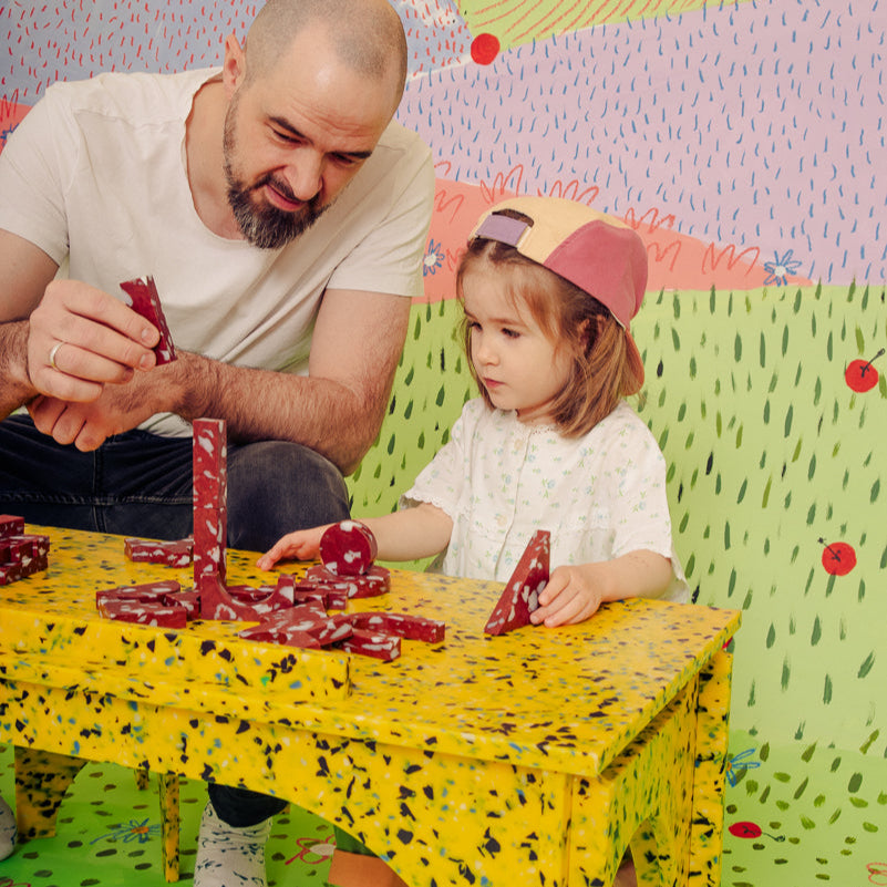 FATHER AND DAUGHTER PLAYING ON M4N1 BENCH OR KIDS DESK IN SUNBURST YELLOW BY THE MINIMONO PROJECT - BRAND FOR ECO FRIENDLY - PLAYFUL - MULTI FUNCTIONAL - SUSTAINABLE - HIGH QUALITY - CIRCULAR DESIGN FURNITURE FROM RECYCLED PLASTIC FOR BOTH ADULT AND CHILDREN MADE IN BERLIN GERMANY
