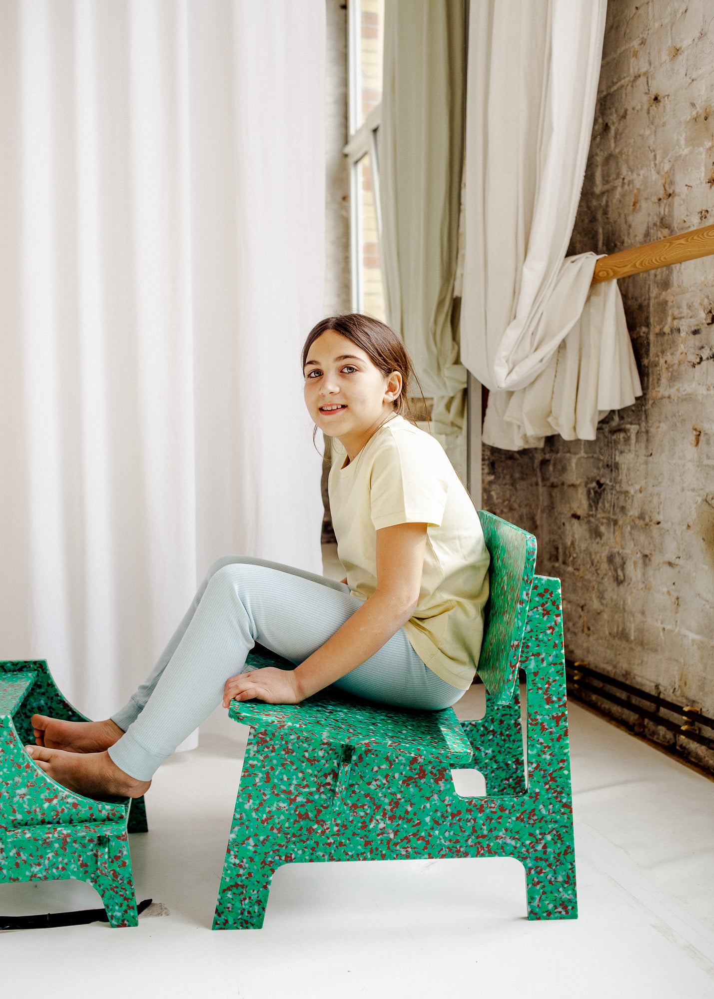SIDE VIEW OF KID SITTING ON GREEN CHAIR BY THE MINIMONO PROJECT - BRAND FOR ECO FRIENDLY - PLAYFUL - MULTI FUNCTIONAL - SUSTAINABLE - HIGH QUALITY - DESIGN FURNITURE FROM RECYCLED PLASTIC FOR BOTH ADULT AND CHILDREN MADE IN BERLIN GERMANY