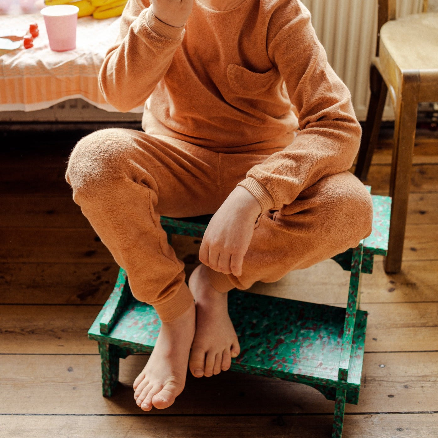 KID SITTING ON GREEN SMALL STEP STOOL BY THE MINIMONO PROJECT - BRAND FOR ECO FRIENDLY - PLAYFUL - MULTI FUNCTIONAL - SUSTAINABLE - HIGH QUALITY - DESIGN FURNITURE FROM RECYCLED PLASTIC FOR BOTH ADULT AND CHILDREN MADE IN BERLIN GERMANY