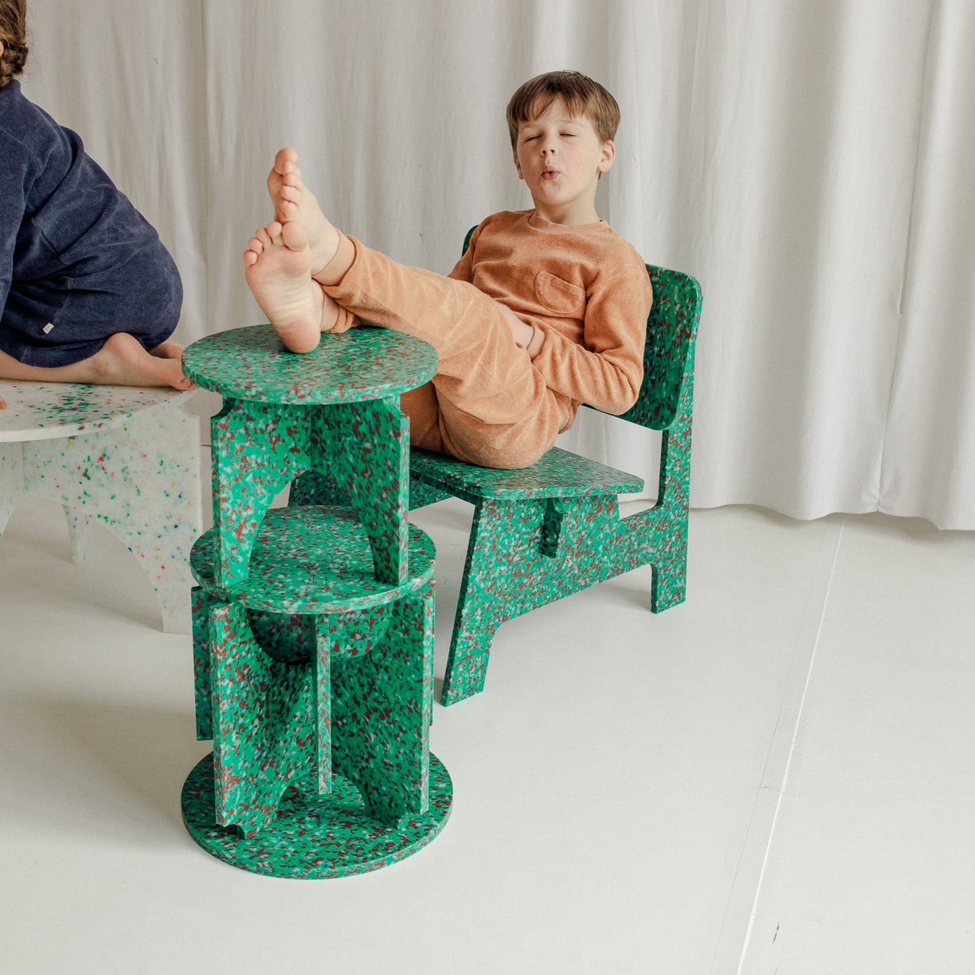 KID SITTING ON GREEN CHAIR BY THE MINIMONO PROJECT - BRAND FOR ECO FRIENDLY - PLAYFUL - MULTI FUNCTIONAL - SUSTAINABLE - HIGH QUALITY - DESIGN FURNITURE FROM RECYCLED PLASTIC FOR BOTH ADULT AND CHILDREN MADE IN BERLIN GERMANY